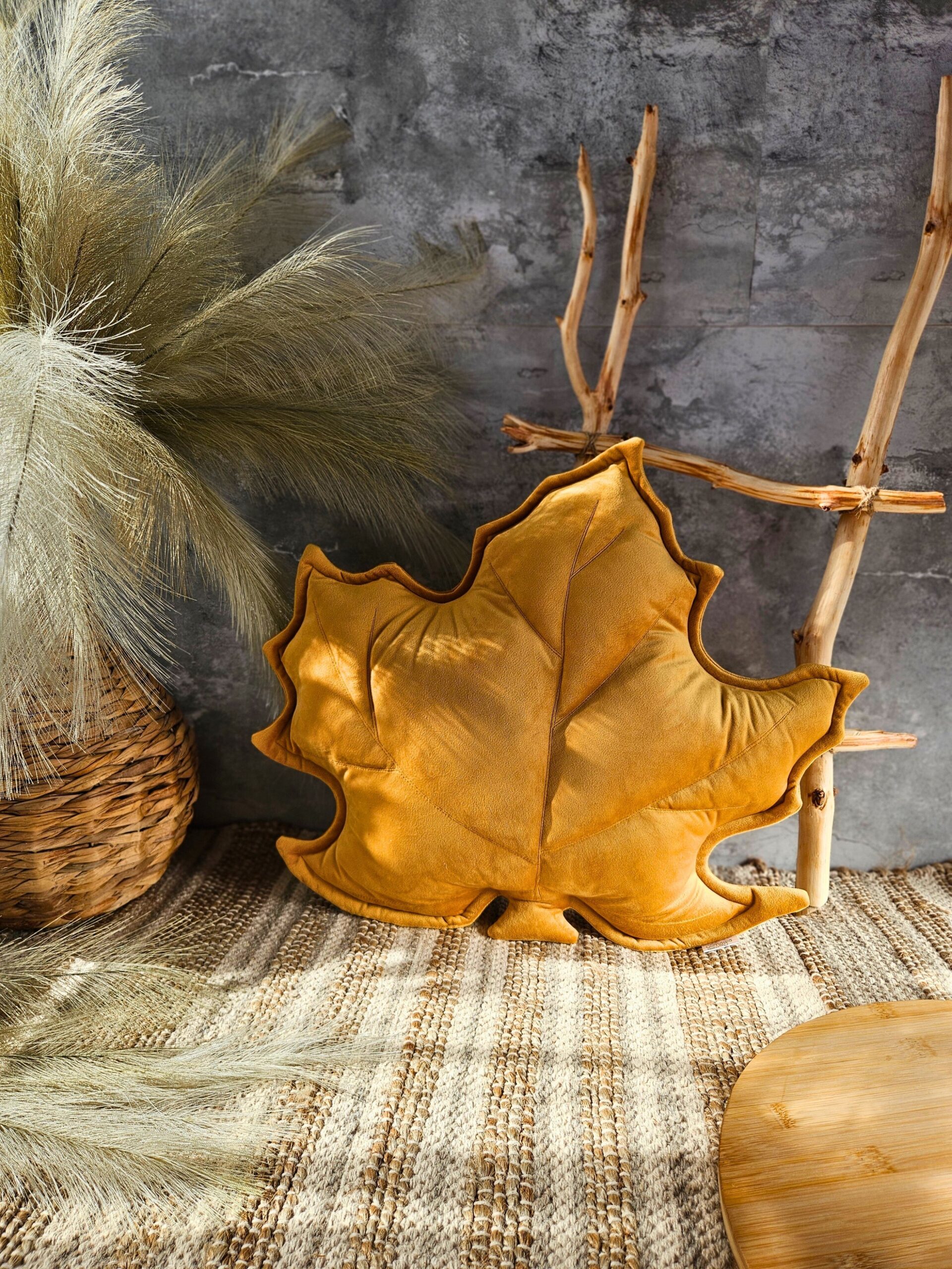 Musztardowa poduszka dekoracyjna w kształcie liścia klonu na szarej kanapie - sposób na przytulny salon.