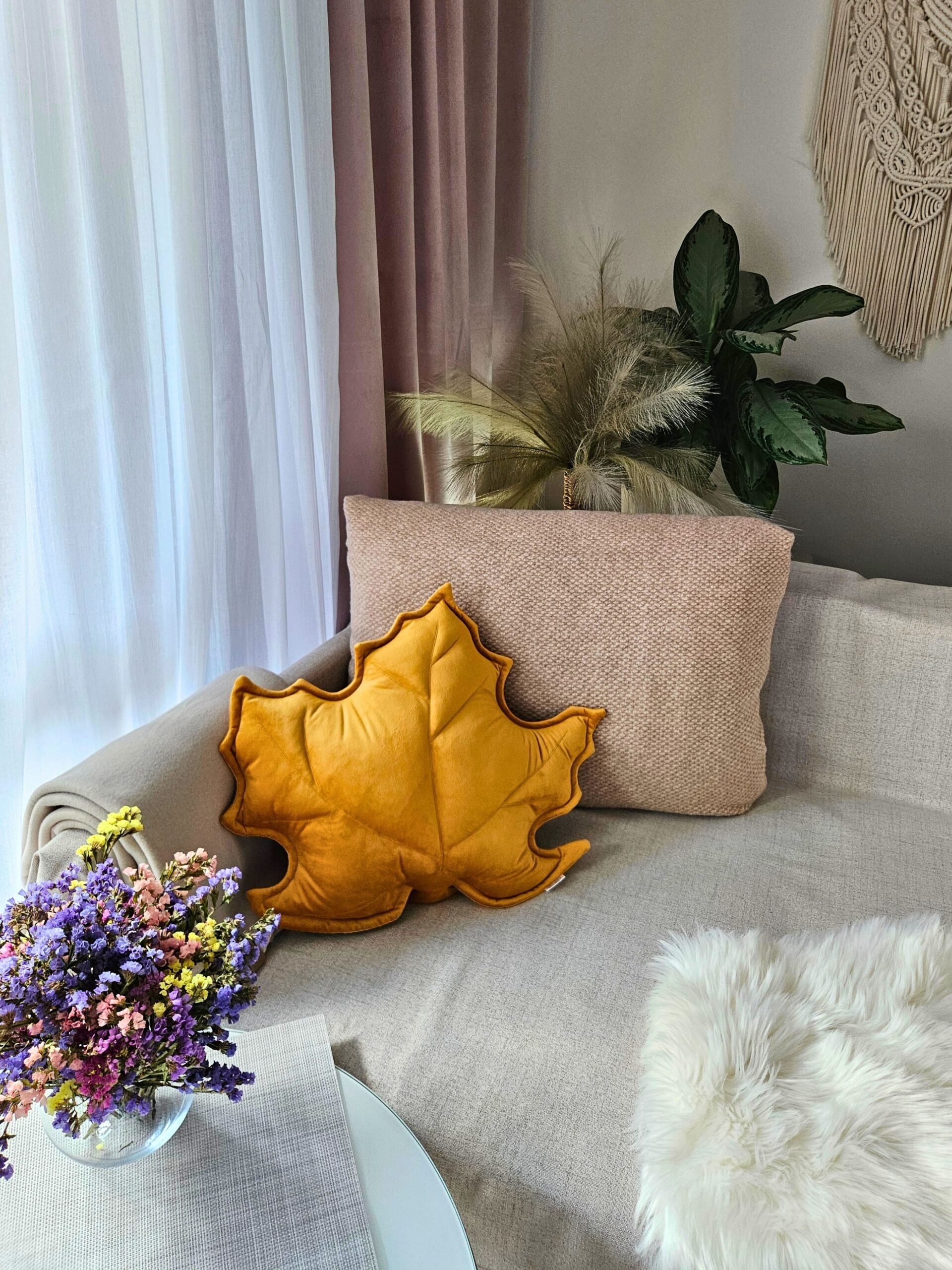 Musztardowa poduszka dekoracyjna w kształcie liścia klonu na szarej kanapie - sposób na przytulny salon.