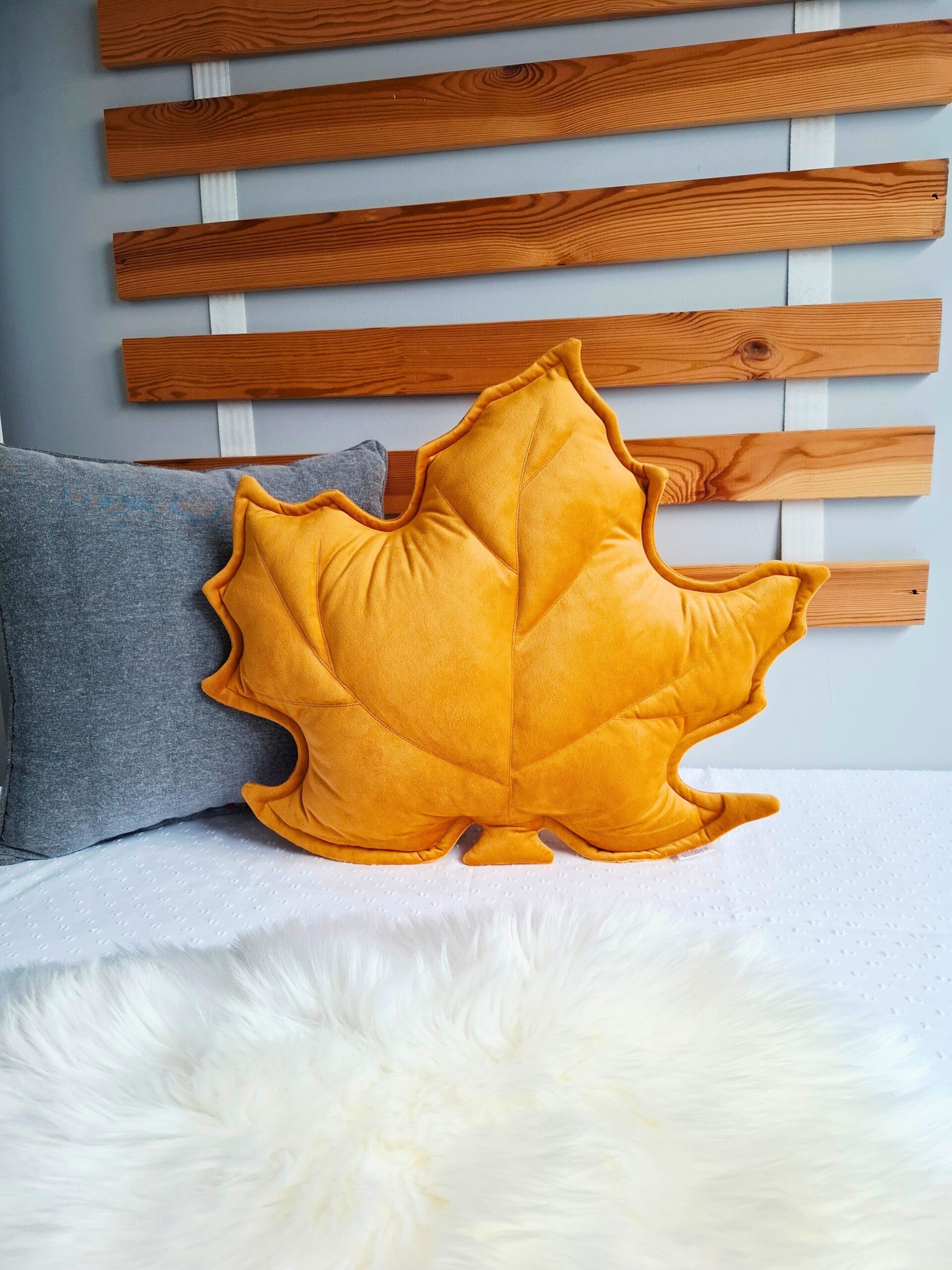 Musztardowa poduszka dekoracyjna w kształcie liścia klonu na szarej kanapie - sposób na przytulny salon.