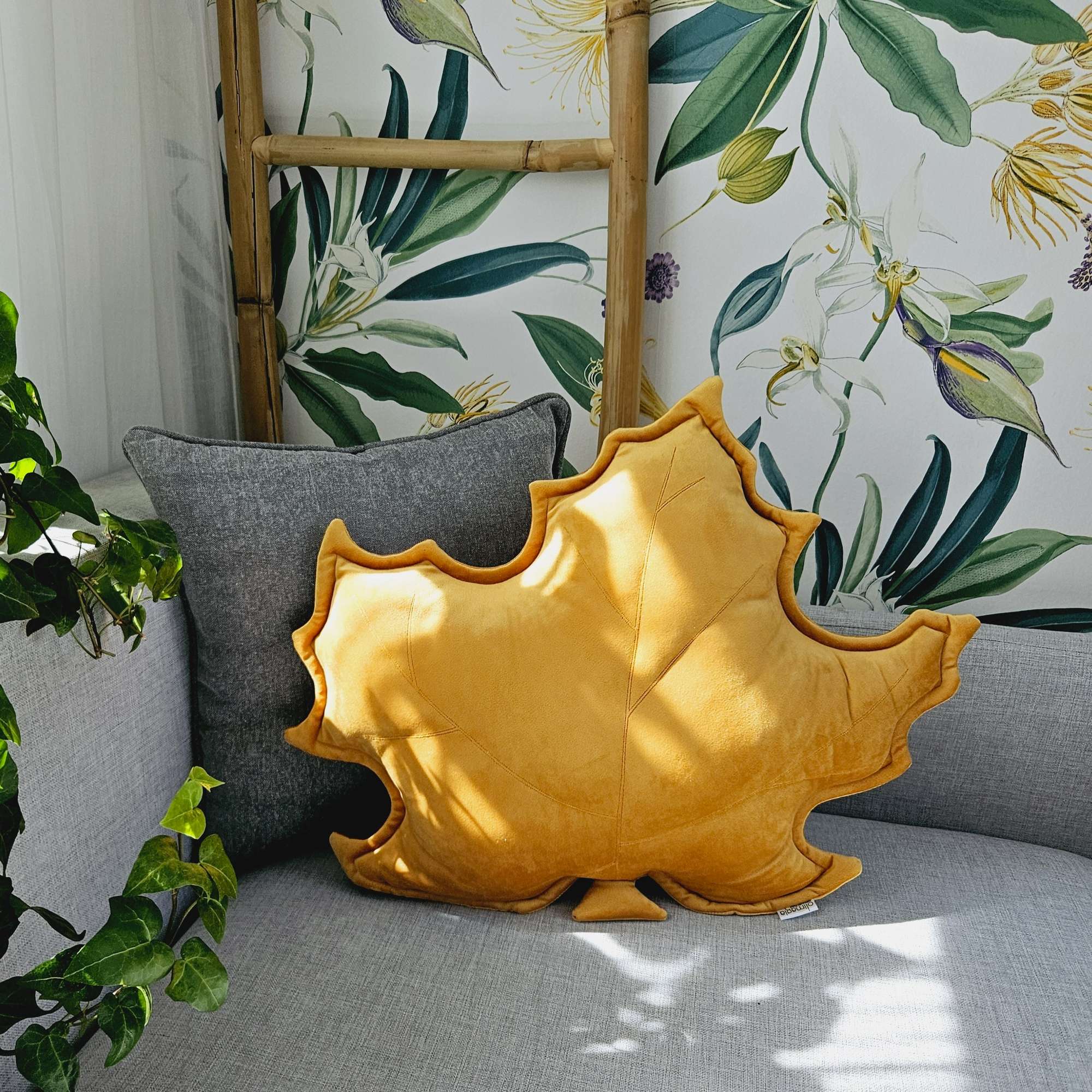 Musztardowa poduszka dekoracyjna w kształcie liścia klonu na szarej kanapie - sposób na przytulny salon.