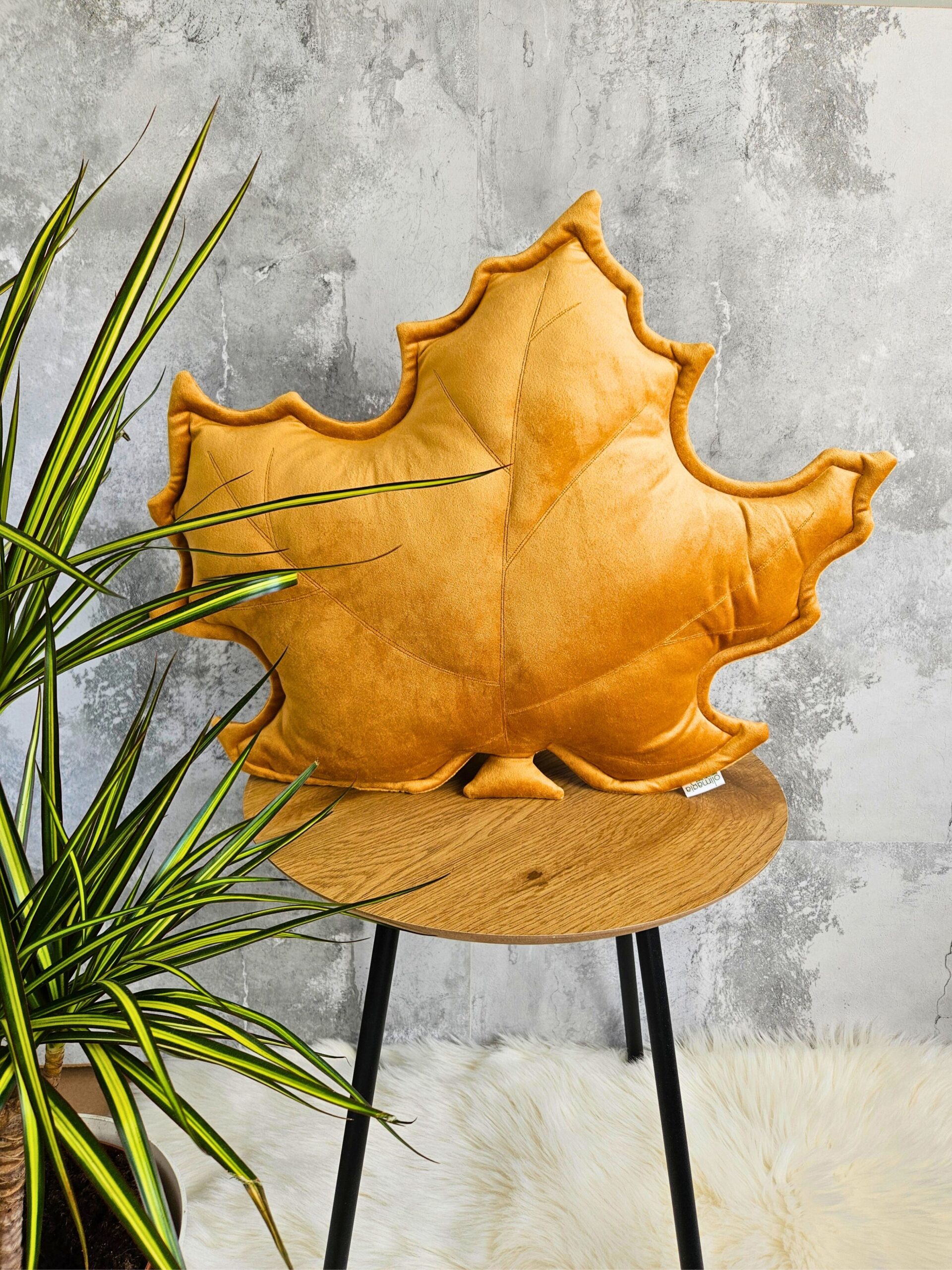 Musztardowa poduszka dekoracyjna w kształcie liścia klonu na szarej kanapie - sposób na przytulny salon.