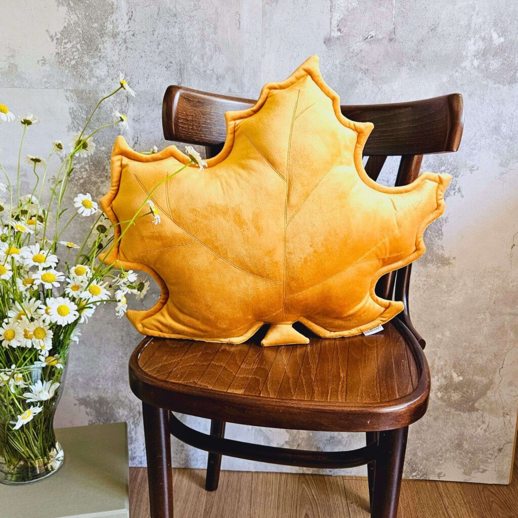 Musztardowa poduszka dekoracyjna w kształcie liścia klonu na szarej kanapie - sposób na przytulny salon.