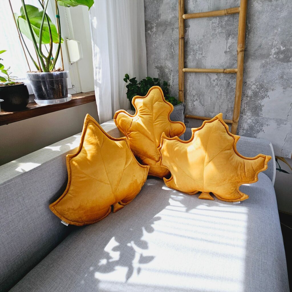 Zestaw poduszek dekoracyjnych do salonu w kształcie kolorowych liści ułożony na jasnej sofie – przytulna aranżacja wnętrza.